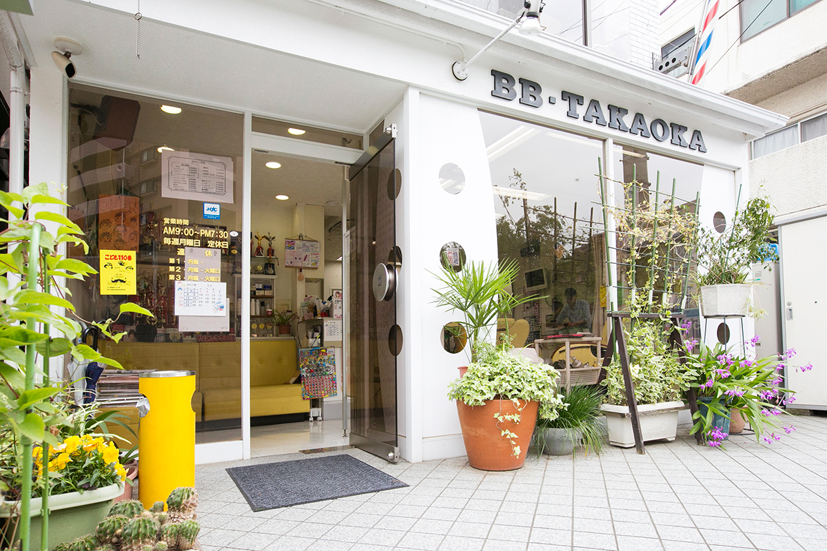 BB TAKAOKAの店舗外観・黄色いサインと観葉植物が目印の入口