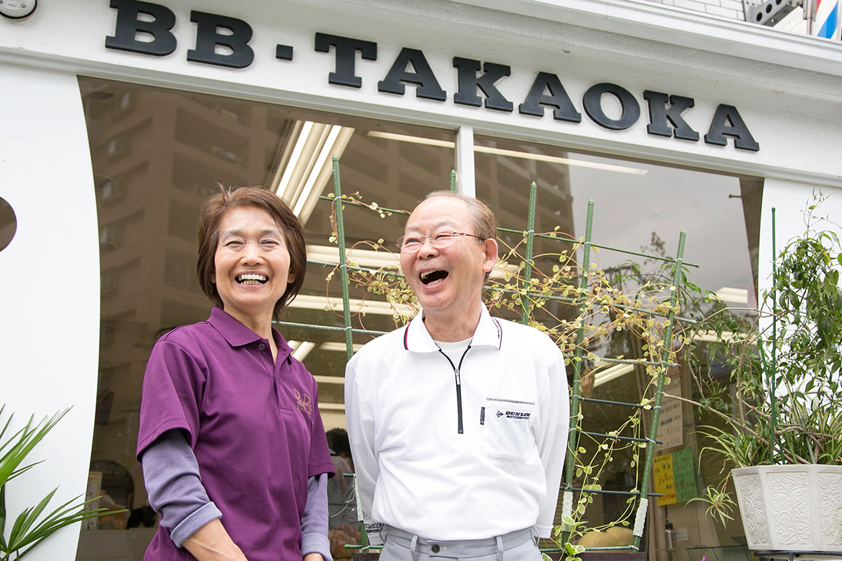 店主夫妻が店頭で笑顔（BB・TAKAOKAの看板の下）